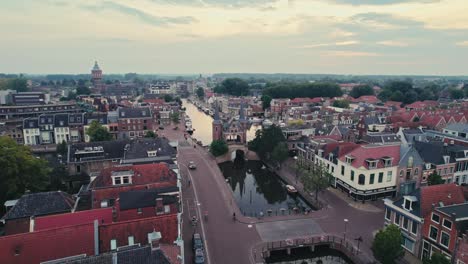 Eine-Europäische-Stadt-In-Der-Abenddämmerung-Mit-Historischen-Gebäuden-Entlang-Eines-Ruhigen-Kanals,-Sanfte-Beleuchtung,-Luftaufnahme