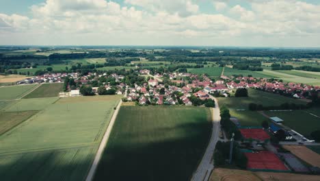 Ein-Malerisches-Dorf,-Umgeben-Von-üppigen-Grünen-Feldern-Unter-Einem-Blauen-Himmel,-Luftaufnahme