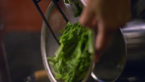 Green-vegetables-being-strained-of-water-using-metal-strainer-and-tongs,-filmed-as-vertical-closeup-slow-motion-shot