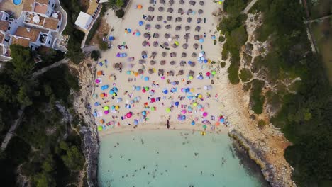 Retreating-overhead-drone-shot-of-the-beachfront-of-Cala-Anguila,-a-cove-located-in-the-island-of-Mallorca-off-the-coast-of-Spain-in-the-Mediterranean-Sea
