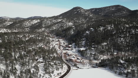 Downtown-old-historic-Evergreen-Colorado-aerial-drone-cinematic-winter-fresh-snow-cold-white-scenic-landscape-near-dam-lake-traffic-driving-around-house-ice-skating-late-morning-blue-sky-upward-motion