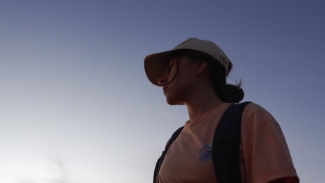 Backpacker-young-woman-with-cap-and-bag-looking-to-horizon-under-clear-sky