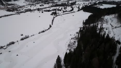 Vista-Aérea-De-La-Pista-De-Carreras-Cubierta-De-Nieve-Cerca-De-La-Ladera-Con-Bosque-Oscuro