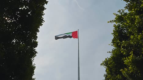 The-UAE-flag-waves-among-greenery-at-Abu-Dhabi-Corniche,-symbolizing-a-sustainable-future-in-the-United-Arab-Emirates