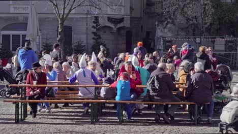 People-in-costumes-sit-on-benches-at-tables-in-a-festival-area-during-the-Gnoccolada-carnival-in-the-city-center-of-Brixen---Bressanone,-South-Tyrol-Italy