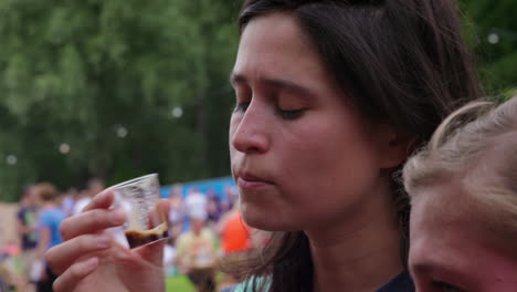 Close-up-of-adult-woman-tasting-dark-beer-in-small-plastic-cup-at-beer-festival