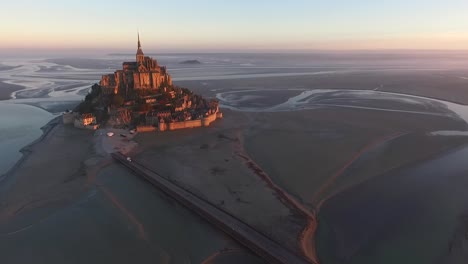 Mont-Saint-Michel-and-bay-at-sunset-with-bridge-connecting-coast-at-island,-Normandy-in-France