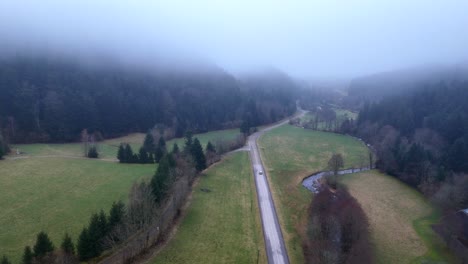 Drone-shot-following-a-distant-car-over-an-ethereal-moody-mountain-landscape-with-fog-and-low-clouds