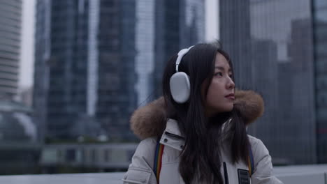 Asian-girl-with-long-black-hair-ang-GUESS-jacket-look-around-in-a-city-with-skyscrapers