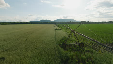Irrigation-system-extends-over-a-green-field-in-Dardanelle,-AR-during-the-day,-mountains-in-distance