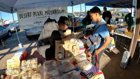 Un-Cliente-Con-Un-Bebé-En-Un-Paquete-Frontal-Está-Comprando-Champiñones-Frescos-En-Un-Puesto-En-El-Mercado-De-Agricultores.