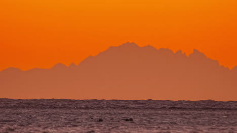 Leuchtend-Orangefarbener-Himmel-über-Einer-Zerklüfteten-Bergkette-Mit-Zeitrafferblick-Auf-Das-Meer