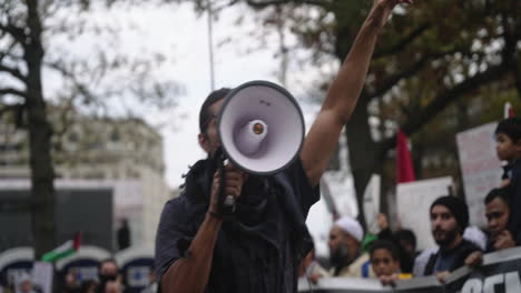 Un-Hombre-Con-Un-Megáfono-Grita-Y-Levanta-El-Puño-Frente-A-Una-Fila-De-Manifestantes-Pro-Palestinos-Alineados-En-La-Calle