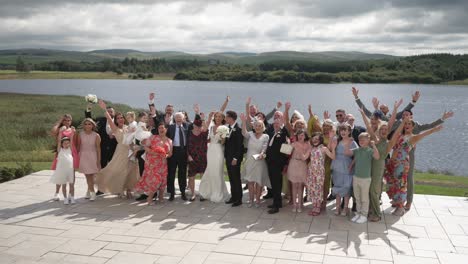 Idyllic-lake-venue-backdrop,-wedding-party-helping-couple-celebrate