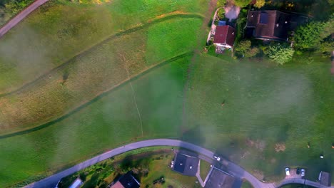 Aerial-view-of-a-rural-landscape-with-patchwork-fields-of-green,-gold,-and-brown,-a-meandering-river,-and-several-farmhouses-with-red-roofs-and-tractor-driving