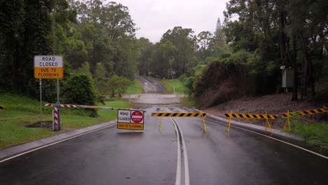 Gold-Coast,-Queensland,-16-February-2024---Wide-shot-of-road-closure-signage-with-flooding-across-Hardy's-Road-in-Mudgeeraba-after-heavy-rains-continue-to-lash-South-East-Queensland,-Australia