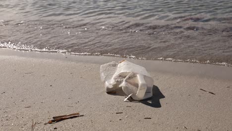 Discarded-plastic-container-with-gentle-waves-in-background,-environmental-pollution-theme
