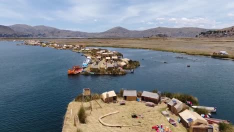 Drohnen-Luftaufnahme-In-Peru,-Die-An-Einem-Sonnigen-Tag-über-Huros-Siedlungen-Auf-Kleinen-Inseln-Mit-Kleinen-Booten-Und-Künstlichen-Häusern-Im-Titikaka-See-In-Puno-Fliegt