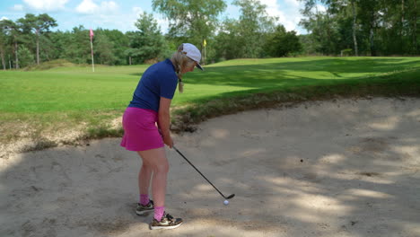 Colourful-young-adult-female-golfer-chipping-golf-ball-out-of-sand-trap-hazard