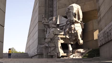 Woman-walking-by-impressive-brutalist-sculpture-of-horse-outside-Bulgarian-State-Monument,-Shumen