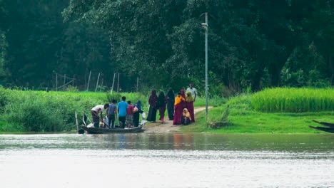 Rural-people-crossing-a-river-in-a-wooden-boat,-with-verdant-fields-in-the-backdrop