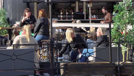 Women-sit-at-outdoor-bar-in-Stockholm,-man-with-face-mask-walks-in-foreground