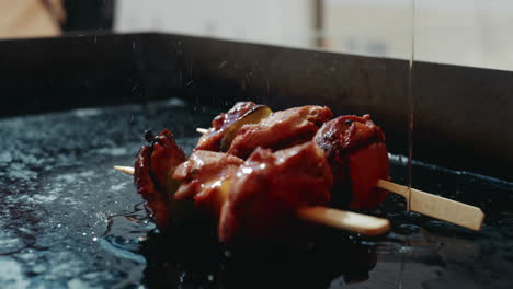 Pouring-fresh-oil-onto-skewers-sitting-on-festival-grill