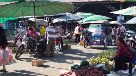 A-view-of-an-open-air-market-where-vendors-exhibit-their-produce-on-the-ground,-while-shoppers'-motorcycles-and-sun-umbrellas-dot-the-scene