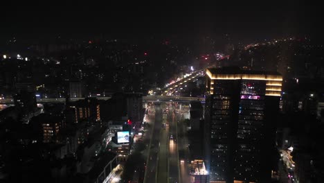 Vista-Aérea-De-Drones-De-Rajkot-Más-Adelante,-Donde-Brillan-Luces-Frías-En-El-Edificio-Y-Muchas-Son-Visibles-Alrededor