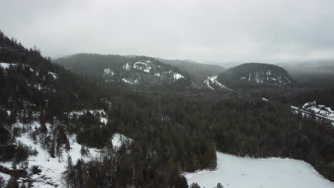 A-aerial-shot-of-mountains-in-the-Adirondacks-with-the-forest-and-a-frozen-lake
