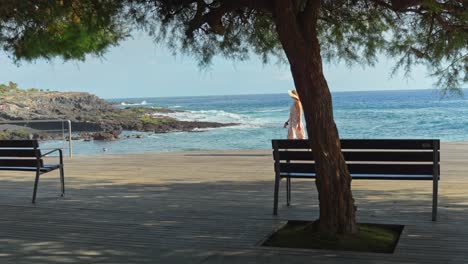 Caucasian-woman-in-a-summer-dress-and-straw-hat-walks-on-coast-of-Mediterranean-sea