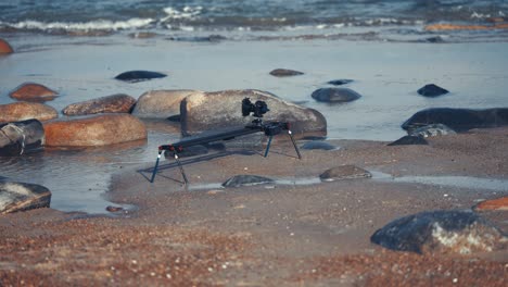 Una-Cámara-Y-Un-Equipo-Deslizante-Instalados-En-La-Playa-De-Arena-Filmando-Las-Olas-Rodando-Hacia-Las-Rocas