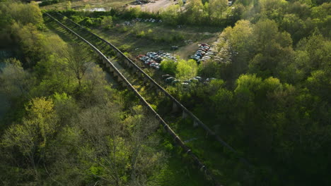 A-junkyard-by-railroad-tracks-in-fayetteville,-ar-during-springtime,-greenery-around,-aerial-view