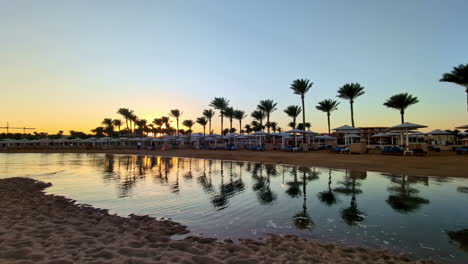 Goldene-Stunde-In-Einem-Ruhigen-ägyptischen-Strandresort-Mit-Palmen-Und-Ruhigem-Wasser,-In-Dem-Sich-Der-Heitere-Himmel-Spiegelt,-Weitwinkelaufnahme