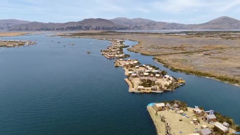 Drone-aerial-view-in-Peru-flying-over-huros-settlements-in-small-islands-with-small-boats-and-manmade-houses-in-the-Titikaka-lake-in-Puno-on-a-sunny-day