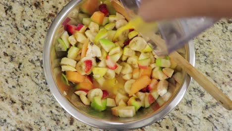 Foto-Superior-De-Una-Mano-Femenina-Vertiendo-Jugo-De-Naranja-Fresco-En-Un-Frutero-Recién-Picado-Sobre-Una-Losa-De-Granito-De-Cocina