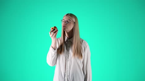 Caucasian-woman-with-glasses-eating-apple,-taking-a-bite,-turquoise-background