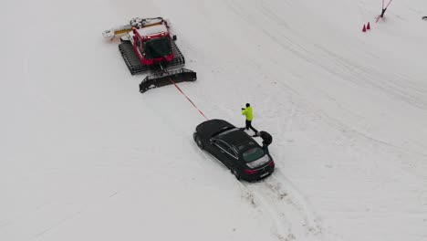 Aerial-view-of-snowcat-pull-out-car-from-snowdrift-at-Lungauring-race-track