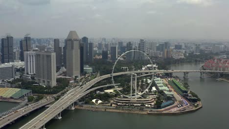 Marina-Bay-Promenade-with-Singapore-Flyer-Next-to-Expressway-and-Cityscape-Background-from-a-Panning-Aerial-Drone