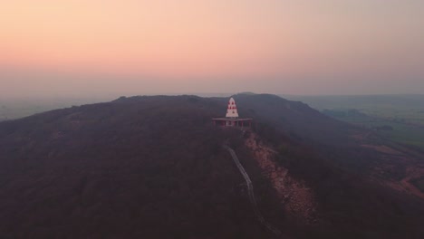 Toma-Aérea-De-Un-Templo-Hindú-En-La-Cima-De-Una-Colina-Con-Escaleras-Que-Conducen-A-él-Durante-La-Puesta-De-Sol-En-Un-Pueblo-De-Gwalior-En-Madhya-Pradesh,-India