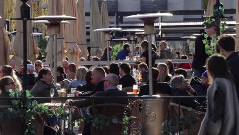 People-drink-at-outdoor-bar-in-Stockholm-during-corona-crisis,-traffic-in-foreground