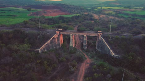 Aerial-drone-shot-of-an-old-concrete-Railway-bridge-with-rail-tracks-with-dense-forest-hills-in-background-during-late-evening-time