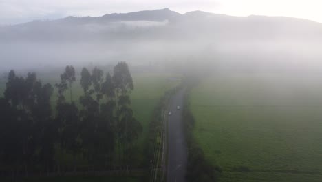 Drone-flight-over-car-the-road-in-thick-fog-on-a-large-grassland-area-with-hills-in-the-background