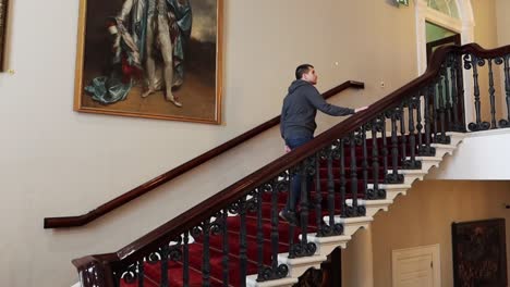 Junger-Mann-Geht-Auf-Altmodischen-Treppen-Mit-Künstlerischen-Gemälden-Im-Hintergrund-Im-Dublin-Castle