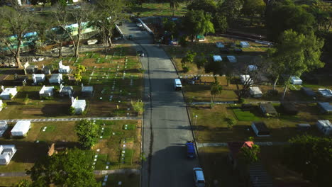 Drone-tilting-over-a-road-in-middle-of-graves-in-Manila-memorial-park,-Philippines