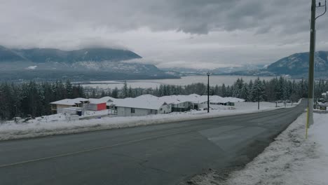 Schwenkaufnahme-Eines-Wohnviertels-Im-Winter-Mit-See-Und-Bergen-Im-Hintergrund