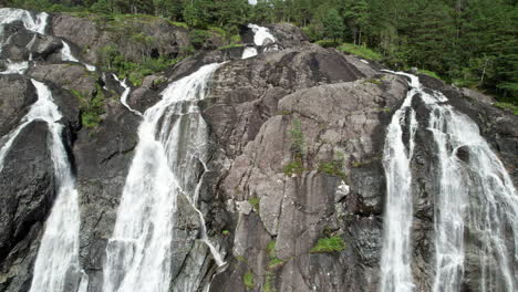 Long-aerial-dolly-shot-pulling-out-from-the-top-of-Laukelandsfossen-Waterfall-in-Norway,-revealing-a-wide-waterfall-with-many-streams-of-water-cascading-over-the-rocky-cliff-face