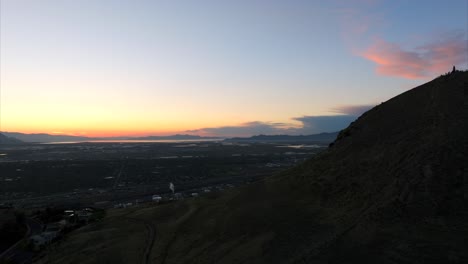 Drone-rising-on-hill-with-Salt-Lake-City-industrial-area-in-background-at-sunset,-Utah-in-USA