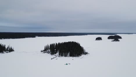 An-outdoor-Drone-Shot-of-an-Island-on-Frozen-Canadian-Paint-Lake-with-an-Ice-fishing-hut-and-skioos
