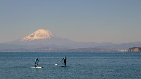 People-enjoying-Stand-up-paddling-in-ocean-with-backdrop-of-Mount-Fuji